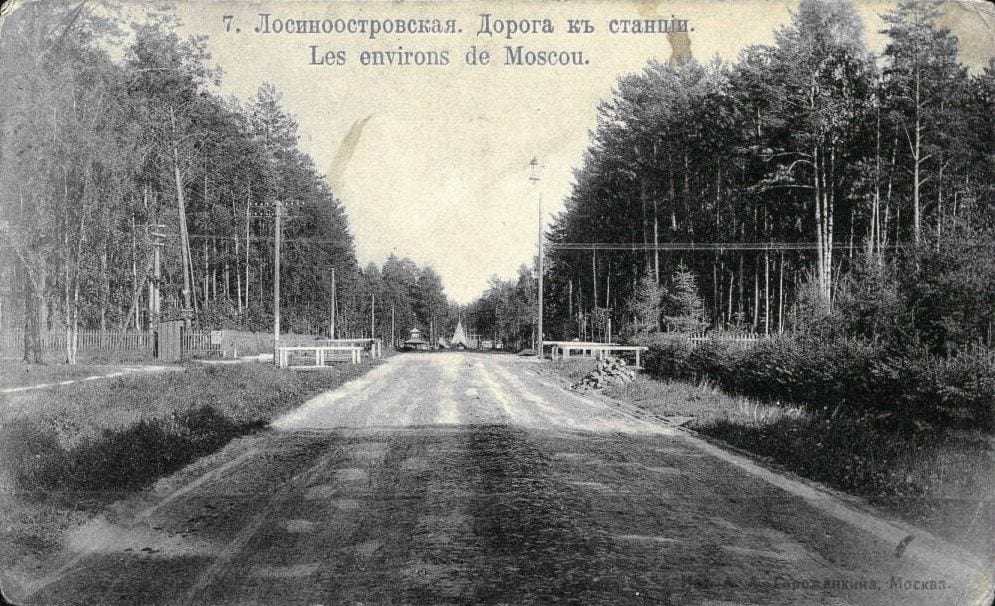 Дорога к станции в дачном посёлке Лосиноостровская, в конце просеки видна островерхая крыша станции. Открытка из серии «Окрестности Москвы». По сопоставлению открыток на pastvu, это Лосиноостровский проезд, нынешняя улица Рудневой, 1900–1910