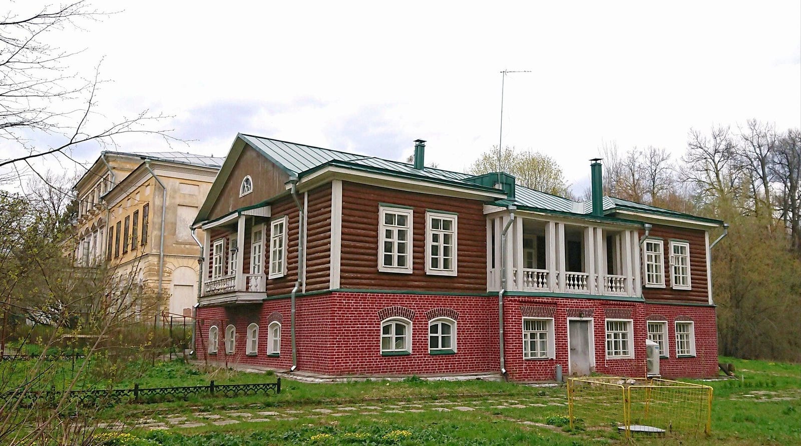 Деревянный флигель 1900-х годов на кирпичном этаже, памятник регионального значения. Слева виден главный дом. май 2021
